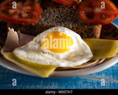 Au petit déjeuner, des oeufs avec le pain sans gluten, fromage, jambon et tomate, sur une table en bois bleu Banque D'Images