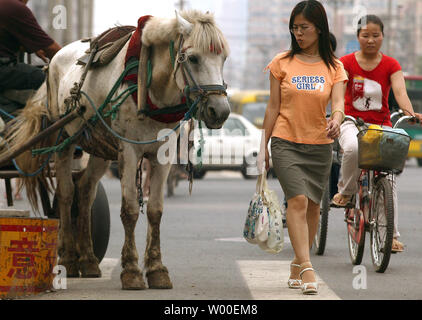 Une femme chinoise passe devant un cheval tirant une charrette de fruits à vendre dans le centre de Pékin, Chine, le 22 juin 2006 Pékin, comme beaucoup de grandes villes de la Chine, est un conte de deux villes ; une ville agressive poussant vers un futur, mégalopole high-tech mais toujours très une ville enchaînés à une grande partie de son passé de faible technologie. (UPI Photo/Stephen Shaver) Banque D'Images