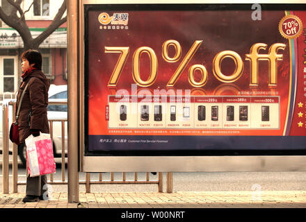 Une femme chinoise attend un bus à côté d'un magasin d'électronique, de la publicité extérieure d'énormes rabais pour les téléphones mobiles et appareils à Beijing le 29 novembre 2009. La croissance de l'économie de la Chine a des représentants du gouvernement de penser à la même sorte de bulle économique que l'Amérique a connu. Avec l'inondation d'argent l'économie chinoise, l'inflation augmente et les consommateurs commencent à dépenser au-delà de leurs moyens, mobiliser eux-mêmes à crédit. UPI/Stephen Shaver Banque D'Images