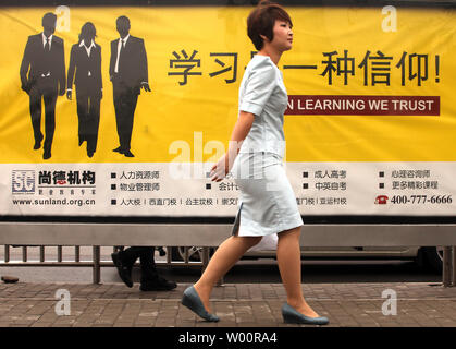 Une femme chinoise passe devant un arrêt de bus des panneaux publicitaires de cours particuliers en affaires et des compétences linguistiques à Pékin le 12 juillet 2010. Capitale de la Chine est devenue la dernière ville du continent désireux de renforcer les compétences en anglais de ses résidents dans le cadre des efforts déployés par le gouvernement pour être plus cosmopolite. Tous les employés du gouvernement en vertu de l'âge de 40 ans seront également tenus de maîtriser au moins 1 000 phrases en français de base pour leur travail quotidien. UPI/Stephen Shaver Banque D'Images