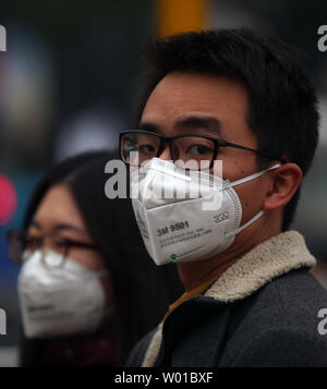 Usure chinois masque de visage pour protéger contre le lourd brouillard qui plane au-dessus de Beijing le 17 novembre 2016. Capitale de la Chine a mis en garde ses 20 millions d'habitants pour limiter les activités de plein air pour éviter les effets néfastes d'une forte pollution couvrant la ville. Photo par Stephen Shaver/UPI Banque D'Images