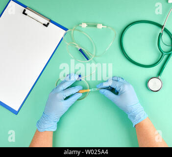 Deux mains du médecin dans des gants bleu tenant une goutte pour injections intraveineuses, fond vert avec un stéthoscope médical Banque D'Images