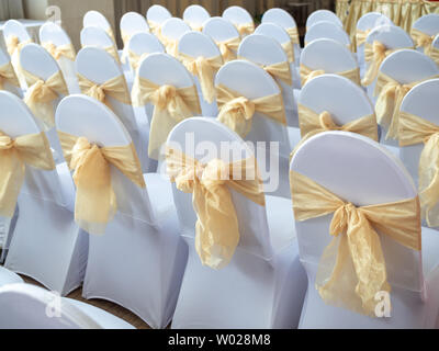 Rangées de belles chaises mariage blanche et propre décoré avec des rubans d'or dans la cérémonie de mariage. Banque D'Images