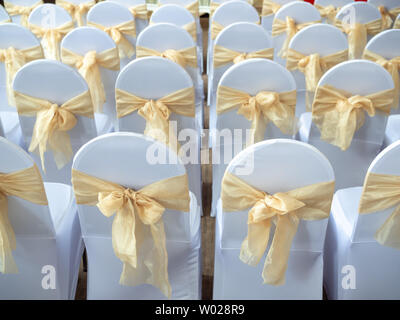 Rangées de belles chaises mariage blanche et propre décoré avec des rubans d'or dans la cérémonie de mariage. Banque D'Images