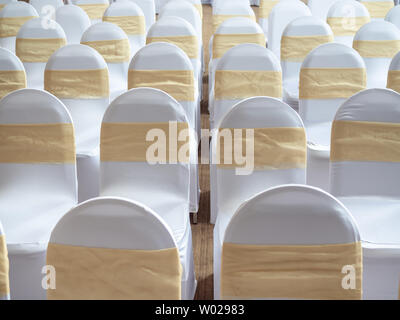 Rangées de belles chaises mariage blanche et propre décoré avec des rubans d'or dans la cérémonie de mariage. Banque D'Images