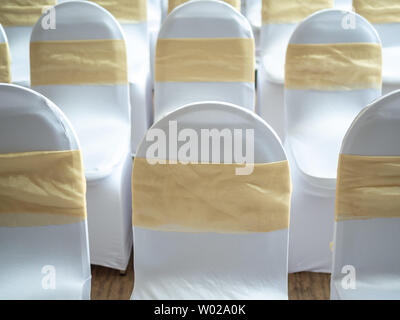 Rangées de belles chaises mariage blanche et propre décoré avec des rubans d'or dans la cérémonie de mariage. Banque D'Images