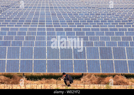 Un Chinois parle sur son téléphone à côté d'un panneau solaire dans le Taiyangshan les champs dans la zone de développement, une ville frontière de Chen dans la province nord-ouest de la région autonome du Ningxia Hui le 22 septembre 2011. Les 215 milles carrés de zone a les avantages de l'énergie éolienne et solaire forte, résultant en 300 mégawatts d'énergie éolienne et 100 MW d'énergie photovoltaïque. Taiyangshan est la plus grande base de l'énergie propre en Chine. UPI/Stephen Shaver Banque D'Images