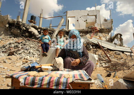 Rowidh al-Najar, est photographié le 21 septembre 2014, la cuisson du pain au milieu des ruines de sa maison à Khan Younis, tandis que ses deux jeunes enfants au sommet les décombres derrière elle. Sa maison, avec ceux de beaucoup d'autres, ont été détruits au cours d'une guerre de sept semaines entre Israël et le Hamas militants dans la bande de Gaza. Selon l'agence des Nations Unies pour l'aide aux réfugiés palestiniens (UNRWA), 65 000 sans-abri palestiniens sont toujours à l'abri dans les écoles de l'ONU en attente d'hébergement et des milliers d'autres ont trouvé refuge chez des parents. Ismael Mohamad/UPI Banque D'Images