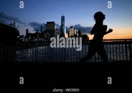 Un jogger s'exécute au coucher du soleil comme en deuil recueillir et attendre pour descendre la piste cyclable en direction de One World Trade Center et le lower Manhattan le long de la West Side Highway participant à une veillée aux chandelles en l'honneur des victimes de la terreur deux jours après jour après un Home Depot chariot claquée par laissant 8 morts et plus d'une douzaine de blessés dans le sud de Manhattan le 2 novembre 2017 à New York. Le suspect en détention, Sayfullo Habibullaevic délibérément, a conduit un camion loué Home Depot sur une longue piste cyclable à proximité du World Trade Center dans le lower Manhattan, tuant huit personnes et sérieusement injurin Banque D'Images