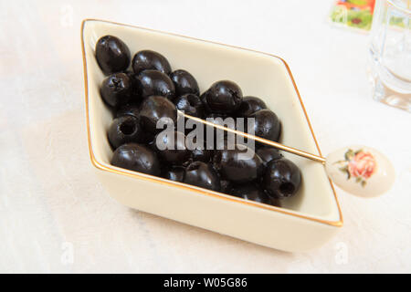 Olive noire de fruits dans un bol en porcelaine avec la fourchette sur nappe blanche. Banque D'Images