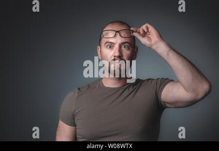 Portrait d'un homme avec l'expression surprise qui soulève ses lunettes, porte une chemise, cliché pris dans le studio. Banque D'Images