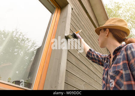 Femme mur extérieur maison en bois peinture avec pinceau et couleur de protection du bois Banque D'Images