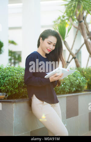 Portrait of smiling female student reading book tout en se tenant en plein air, sur la terrasse de café campus en journée ensoleillée. L'éducation, de vie et de personnes concept Banque D'Images