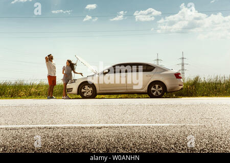 Le jeune couple a enfoncé la voiture tout en voyageant sur la façon de se reposer. Ils essaient de le bris par leurs propres ou en auto-stop, devrait devenir nerveux. Relation, problèmes sur la route, en vacances. Banque D'Images