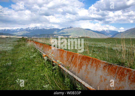 Aryk picotés par lichen sur une vallée verte sur fond de collines et montagnes aux sommets enneigés et un ciel nuageux. Un voyage au Kirghizistan Banque D'Images