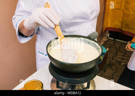 La fabrication du fromage à partir de lait à la maison. Incorporer le levain de main de fromage avec une cuillère dans une casserole. La technologie de la cuisson du fromage. Les processus de fabrication du fromage Banque D'Images