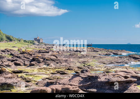 Portencross Bay sur le solstice d'Écossais à la recherche sur la vieille jetée et ruines comme le soleil se couche et d''Ailsa Craig peut être vu dans le ciel voilé dist Banque D'Images