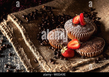 Muffins au chocolat avec des fraises saupoudrées de sucre en poudre sur un sac de jute de grains de café. Banque D'Images