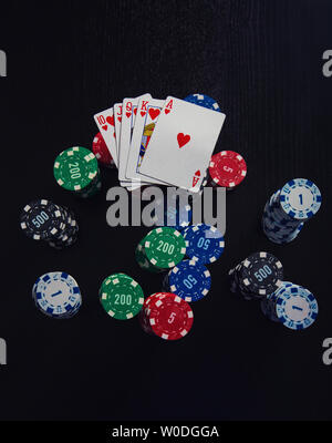 Grande pile de jetons différents et la plus forte combinaison de cartes à jouer au poker - royal flush isolated over black casino table. Le jeu tourname Banque D'Images