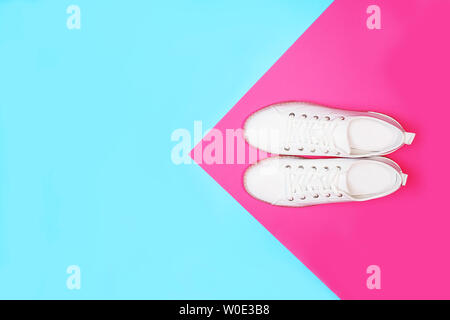 Espadrilles blanches se trouvent sur le néon lumineux couleur bleu rose l'arrière-plan. Banque D'Images