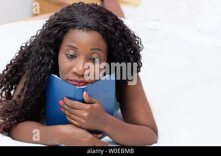 Pensive young woman Lying in Bed avec un livre dans ses mains. Banque D'Images