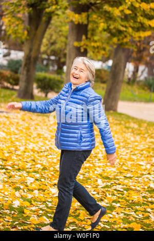 Portrait d'un souriant et expressif senior woman walking à la dynamique de l'étape d'un parc/feuilles jaunes. Banque D'Images