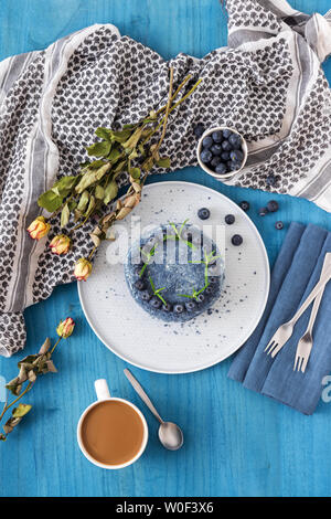 Table avec Myrtille Velvet Cake. Tasse de café avec du lait, un petit bol de myrtilles, d'écharpe et de fleurs sèches, roses. Banque D'Images