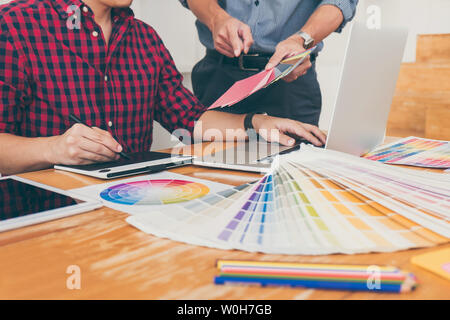 Le travail d'équipe de jeunes designers créatifs travaillant sur l'ensemble du projet et choisir des échantillons de couleur pour colorier sélection numérique sur tablette graphique à w Banque D'Images