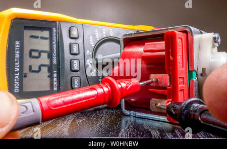 Libre d'un électricien, d'attacher les mains de sondes d'un multimètre numérique pour un petit moteur, pour faire une lecture et vérifier sa fonctionnalité. Banque D'Images