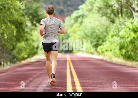 Coureur mâle s'exécutant sur route pour la remise en forme. Homme d'entraînement jogging courir dehors en été dans la nature. Athlète dans des chaussures de course et des courts-circuits pour marathon. Banque D'Images