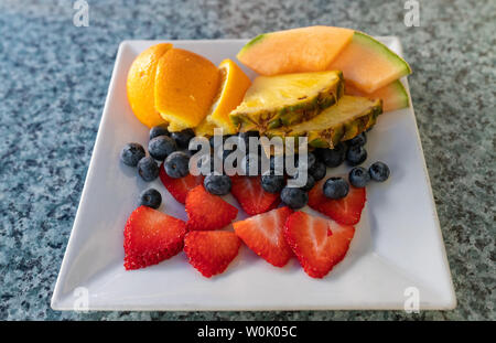 Dessert de fruits frais sur une assiette rectangulaire avec des tranches d'oranges, ananas, melon, les bleuets et les fraises pour un repas santé Banque D'Images