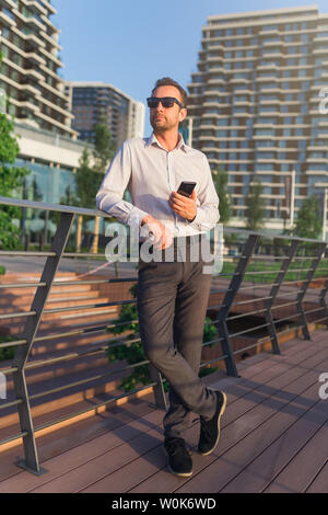 Successful Business Executive en utilisant smartphone outdoors. Les immeubles de bureaux à l'arrière-plan. Banque D'Images