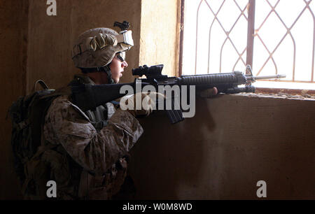 Une des montres marines par une fenêtre tandis que d'autres marines de l'Hawaii, Lima Company, 3e Bataillon, 3e Régiment de Marines, recherchez une maison à Barwana, l'Iraq, de caches d'armes et d'explosifs au cours d'une patrouille dans la ville le 16 juin 2006. Malgré la superbe coup à l'insurrection il y a deux semaines avec la mort d'al-Qaïda en Irak chef Abu Musab al Zarqawi, marines et soldats irakiens dans ce Al Anbar Province ville continuent la lutte contre le terrorisme par la lutte contre les activités des insurgés près de tous les jours. Mais tandis que les Marines et les soldats irakiens patrouillent les rues usées bordée de dépressions Banque D'Images