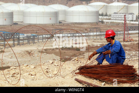 Un travailleur chinois en acier bobines près d'une cour d'entreposage de carburant et d'une usine de gaz liquide en eau profonde dans la toujours underconstruction Jailan port, une grande échelle de l'industrie portuaire globale zone, située à Zhuhai, une ville importante située sur la rivière des Perles dans le sud de la province chinoise du Guangdong le 26 octobre 2013. Jailan port est une configuration de poids lourds et de l'industrie chimique ont porté principalement sur la fabrication et de devenir une industrie pétrochimique et du carburant pour le déchargement de base et de raffinement. BP et Shell ont ouvert de vastes zones dans la zone portuaire. La sécurité des ressources, en particulier l'énergie, est devenue une priorité absolue pour Banque D'Images