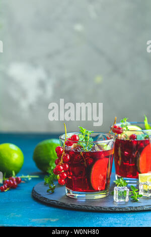 Cocktail rouge froid avec groseille, citron vert, menthe, thym et de glace en verre sur la surface de béton sombre tableau. Été, des boissons et des cocktails sans alcool. Les co Banque D'Images