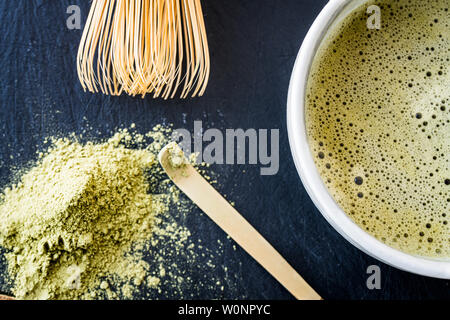 Un gros plan de thé vert matcha dans une tasse, cuillère bambou bambou whist, et le thé vert en poudre Banque D'Images