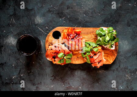 Pour Bruschetta vin. Variété de petits sandwiches servis avec du vin rouge sur la planche de bois rustique sur fond sombre. Vue de dessus avec l'exemplaire de l'espace. Banque D'Images