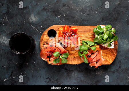 Pour Bruschetta vin. Variété de petits sandwiches servis avec du vin rouge sur la planche de bois rustique sur fond sombre. Vue de dessus avec l'exemplaire de l'espace. Banque D'Images