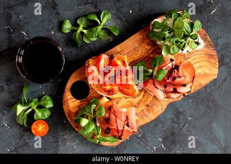 Pour Bruschetta vin. Variété de petits sandwiches servis avec du vin rouge sur la planche de bois rustique sur fond sombre. Vue de dessus avec l'exemplaire de l'espace. Banque D'Images