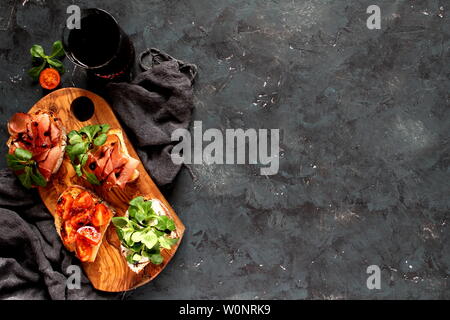 Pour Bruschetta vin. Variété de petits sandwiches servis avec du vin rouge sur la planche de bois rustique sur fond sombre. Vue de dessus avec l'exemplaire de l'espace. Banque D'Images