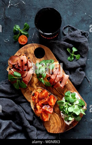 Pour Bruschetta vin. Variété de petits sandwiches servis avec du vin rouge sur la planche de bois rustique sur fond sombre. Vue de dessus avec l'exemplaire de l'espace. Banque D'Images