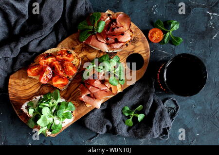 Pour Bruschetta vin. Variété de petits sandwiches servis avec du vin rouge sur la planche de bois rustique sur fond sombre. Vue de dessus avec l'exemplaire de l'espace. Banque D'Images