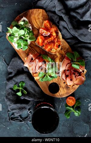 Pour Bruschetta vin. Variété de petits sandwiches servis avec du vin rouge sur la planche de bois rustique sur fond sombre. Vue de dessus avec l'exemplaire de l'espace. Banque D'Images