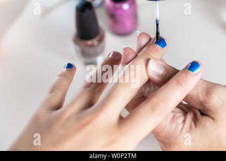 Une mère peint ses mains de jeune fille en bleu et rose nailpolish, considéré dans un cas isolé sur fond blanc Banque D'Images