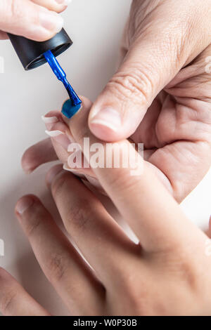 Une mère peint ses mains de jeune fille en bleu et rose nailpolish, considéré dans un cas isolé sur fond blanc Banque D'Images