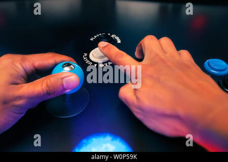 Les mains d'un joueur de jeux vidéo d'atteindre pour le joueur un bouton de démarrage et la tenue d'un sommet à quatre voies de feu joystick. Banque D'Images