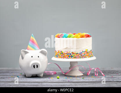 Concept de l'argent d'anniversaire avec gâteau Arc-en-ciel, une bougie et mignon Tirelire sur un fond neutre. Banque D'Images