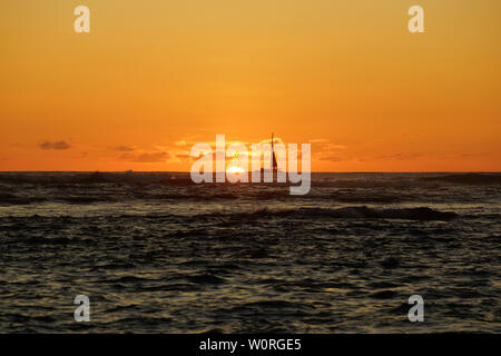 Coucher de soleil sur l'océan avec la lumière se reflétant sur les vagues de l'océan se déplaçant avec des bateaux sur l'eau au loin au large de Waikiki avec nuages sur Oahu, Hawaii. Banque D'Images