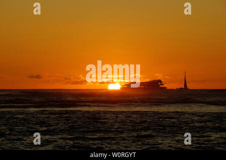 Coucher de soleil sur l'océan avec la lumière se reflétant sur les vagues de l'océan se déplaçant avec des bateaux sur l'eau au loin au large de Waikiki avec nuages sur Oahu, Hawaii. Banque D'Images