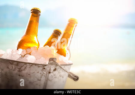 Trois bouteilles de bière en métal seau rempli de glaçons dans la plage de près. Composition horizontale. Vue de face. Banque D'Images